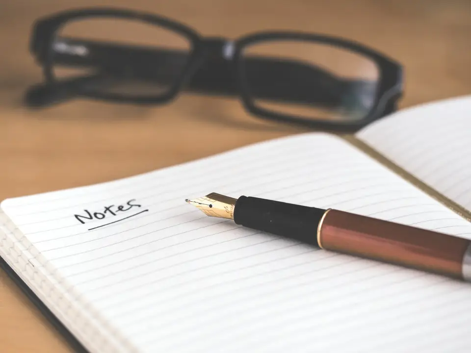 Cuaderno de notas abierto con un bolígrafo y unas gafas sobre una mesa de madera